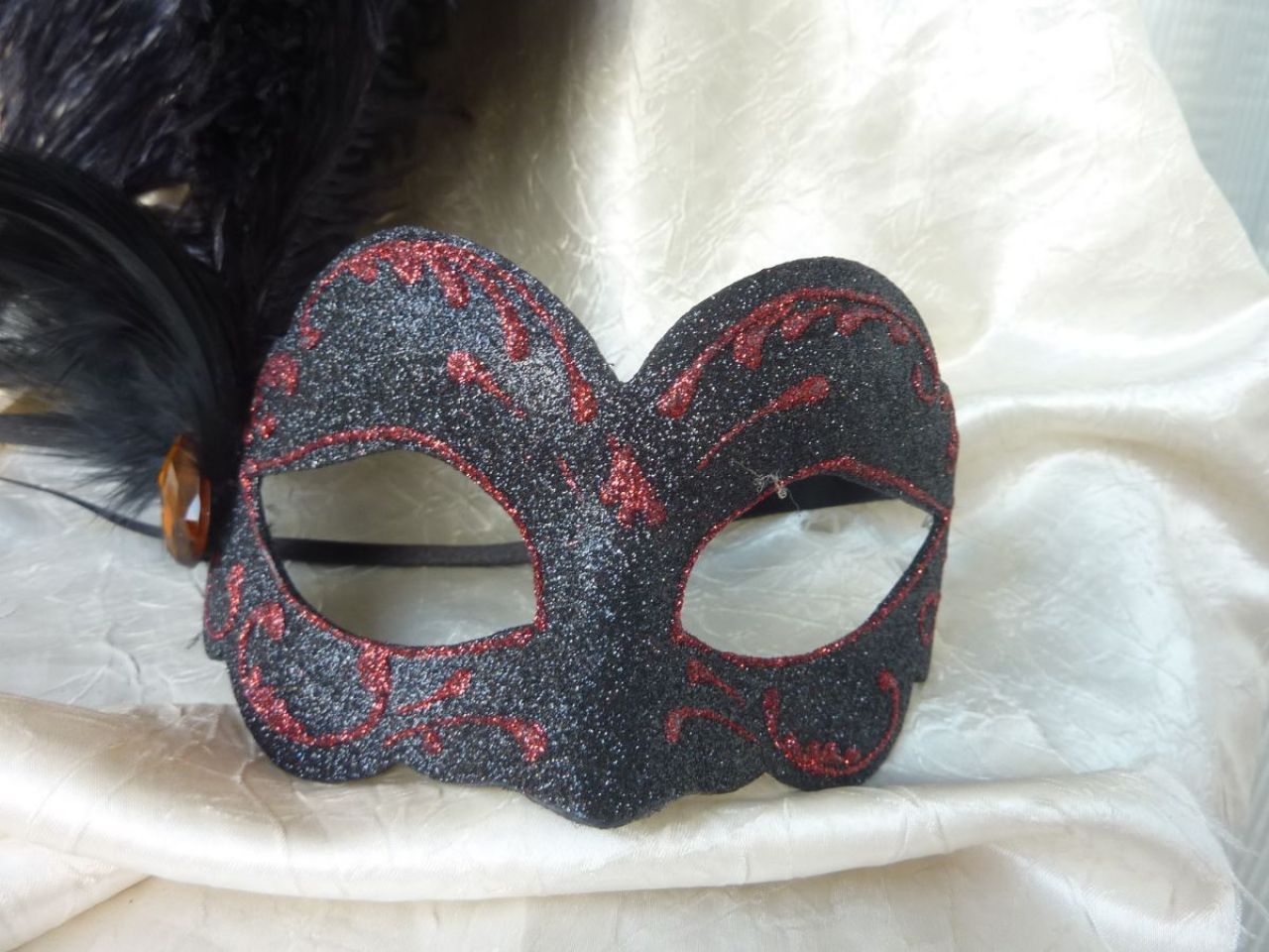 masque loup avec paillettes noir et plumes d'autrouche nois, dessin en glitter rouge, bijou sur le coté