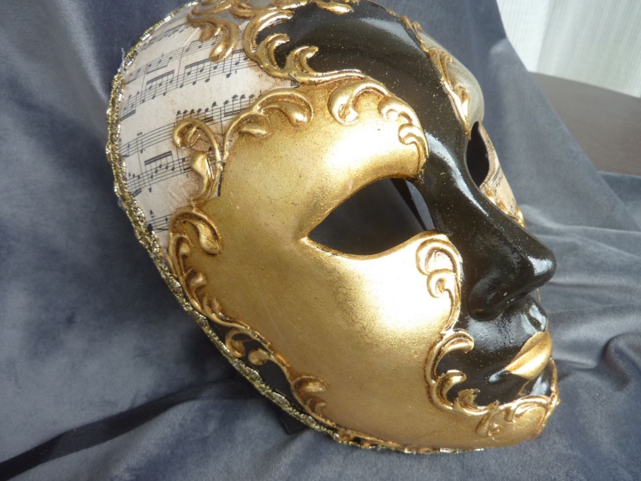 masque visage dessiné à la main, sur fond noir applications de feuilles d'or, cuivre et argent. Reproductions de partitions de musique
